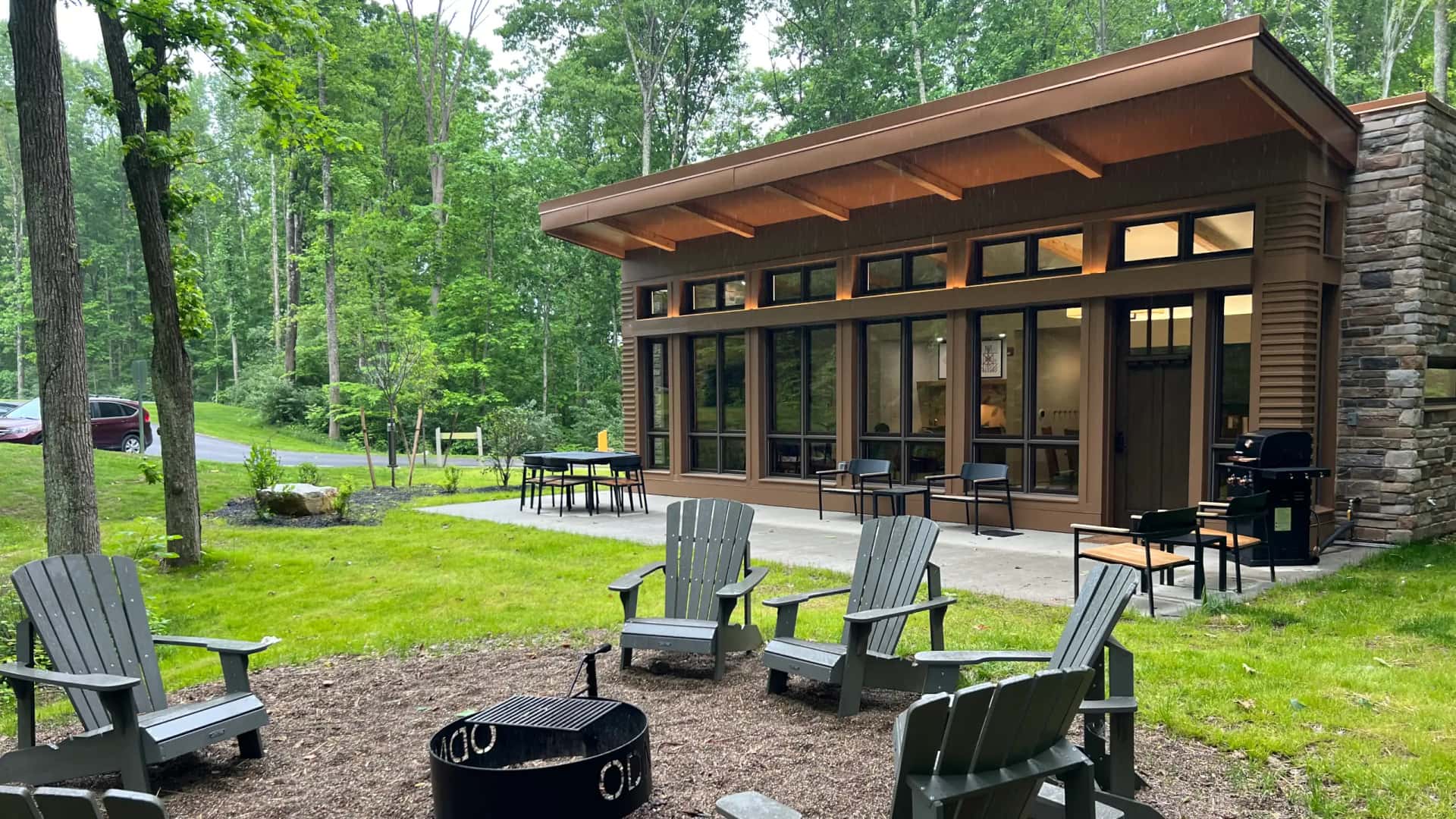 The exterior view of a modern dark brown cabin with massive floor-to-ceiling windows and a concrete patio at Jesse Owens State Park.