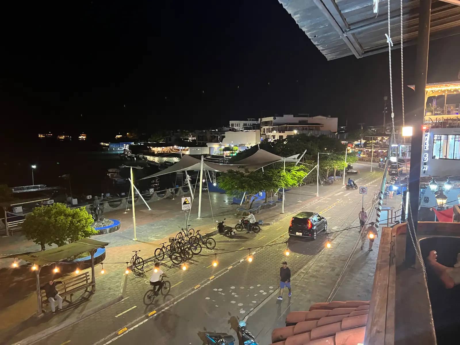 Nighttime view of Puerto Ayora waterfront promenade with string lights and pedestrians from bar balcony Santa Cruz Island Galapagos Islands Ecuador