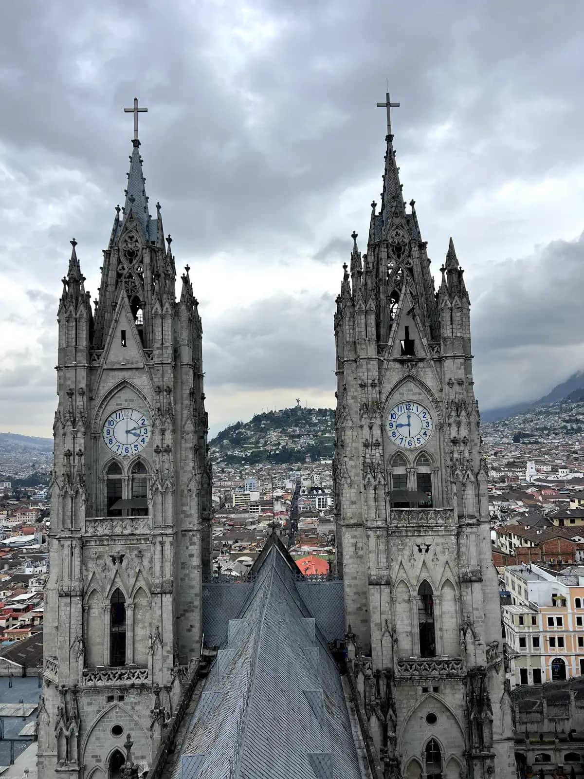 Basílica del Voto Nacional twin Gothic bell towers from viewpoint with Virgen of Quito statue on El Panecillo hill visible between towers Quito Ecuador
