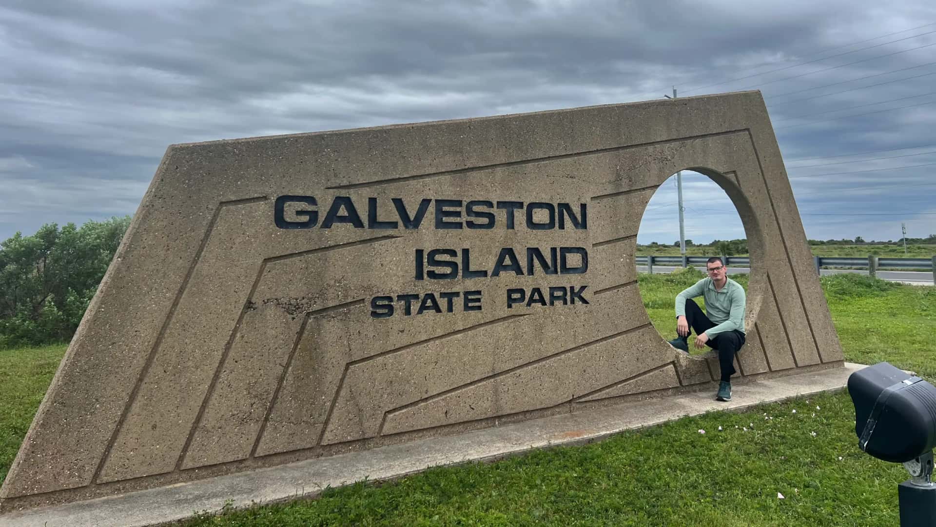 The Lost Shepard sitting beside the Galveston Island State Park entrance sign under a cloudy sky