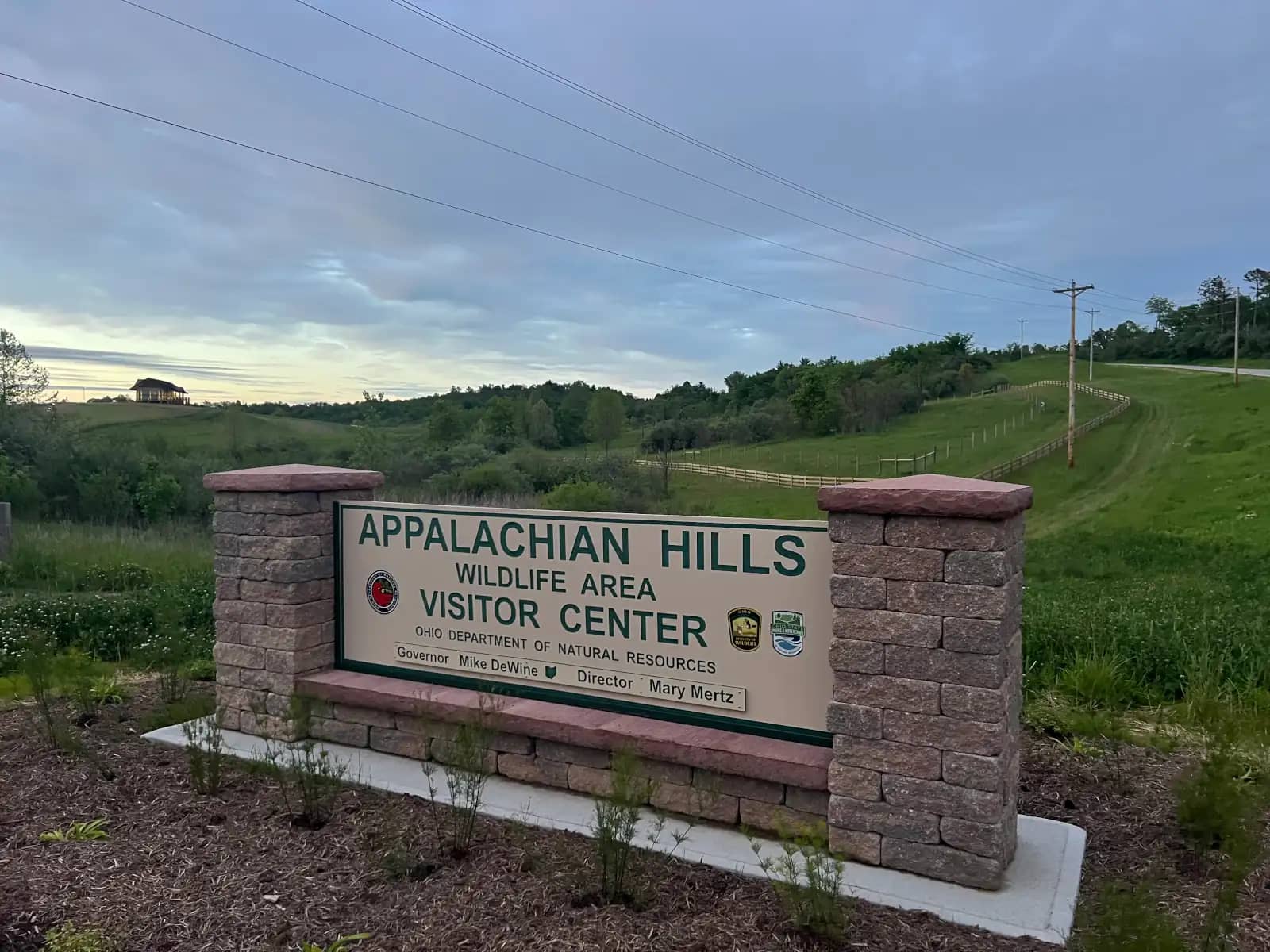 A stone-pillared entrance sign reading "Appalachian Hills Wildlife Area Visitor Center" under an overcast, cloudy sky in rural Ohio.