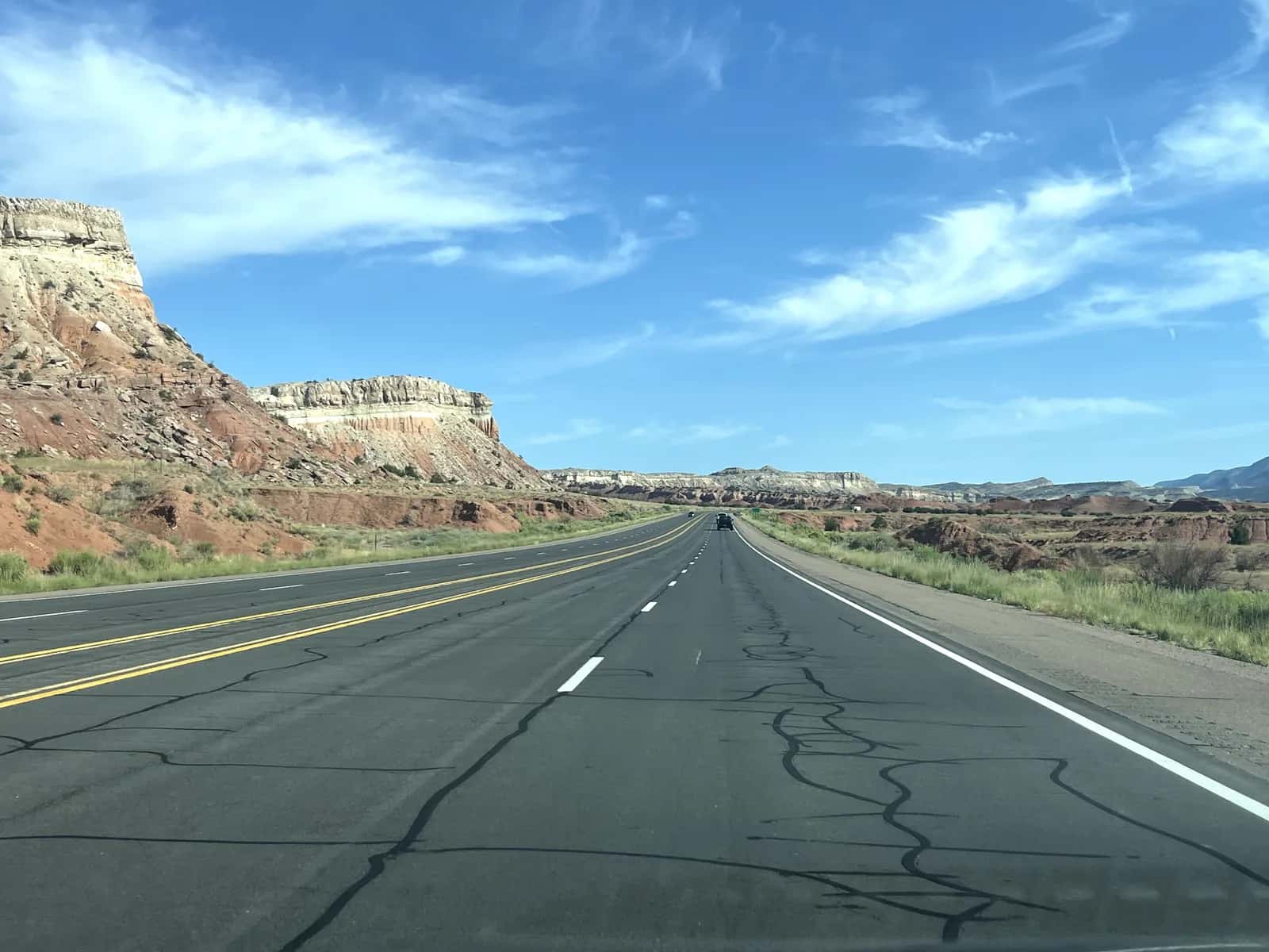Open highway stretching through layered sandstone cliffs and arid desert landscape under a blue sky in the American Southwest