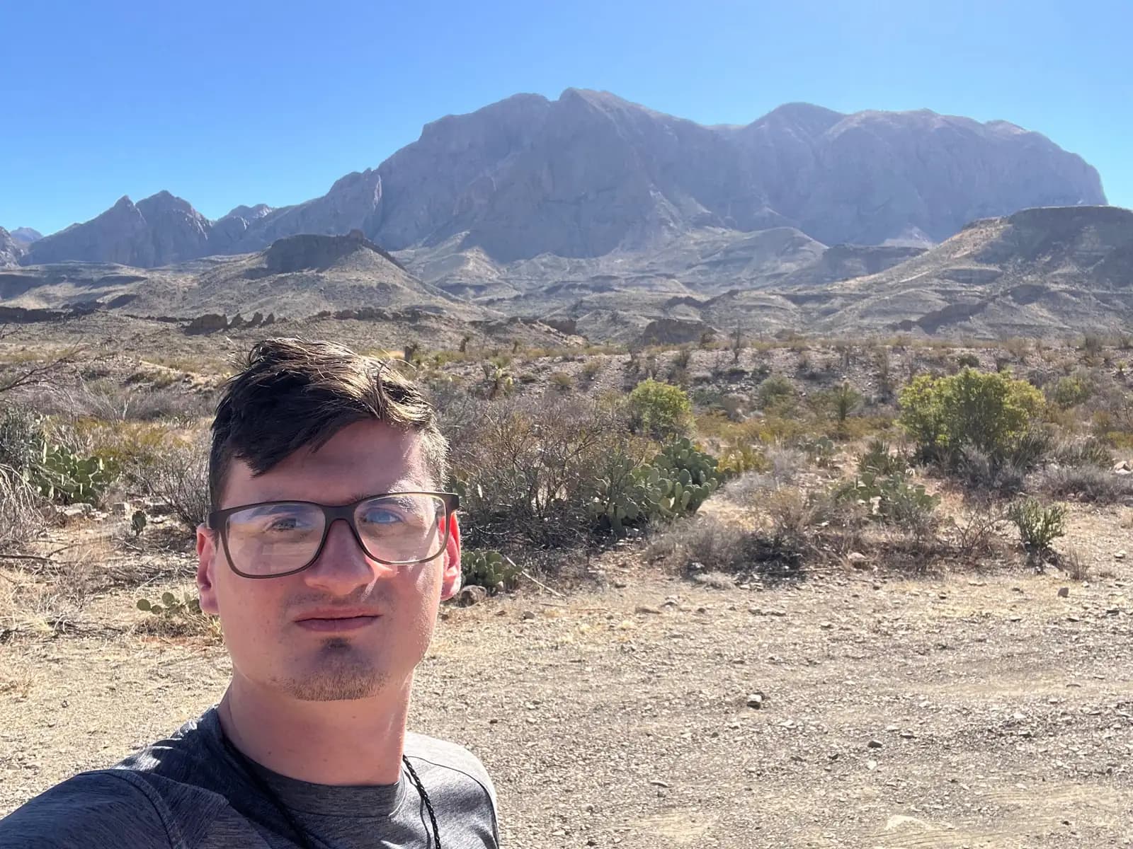 A selfie of a man in glasses with the rugged, sun-drenched Chisos Mountains rising in the background.