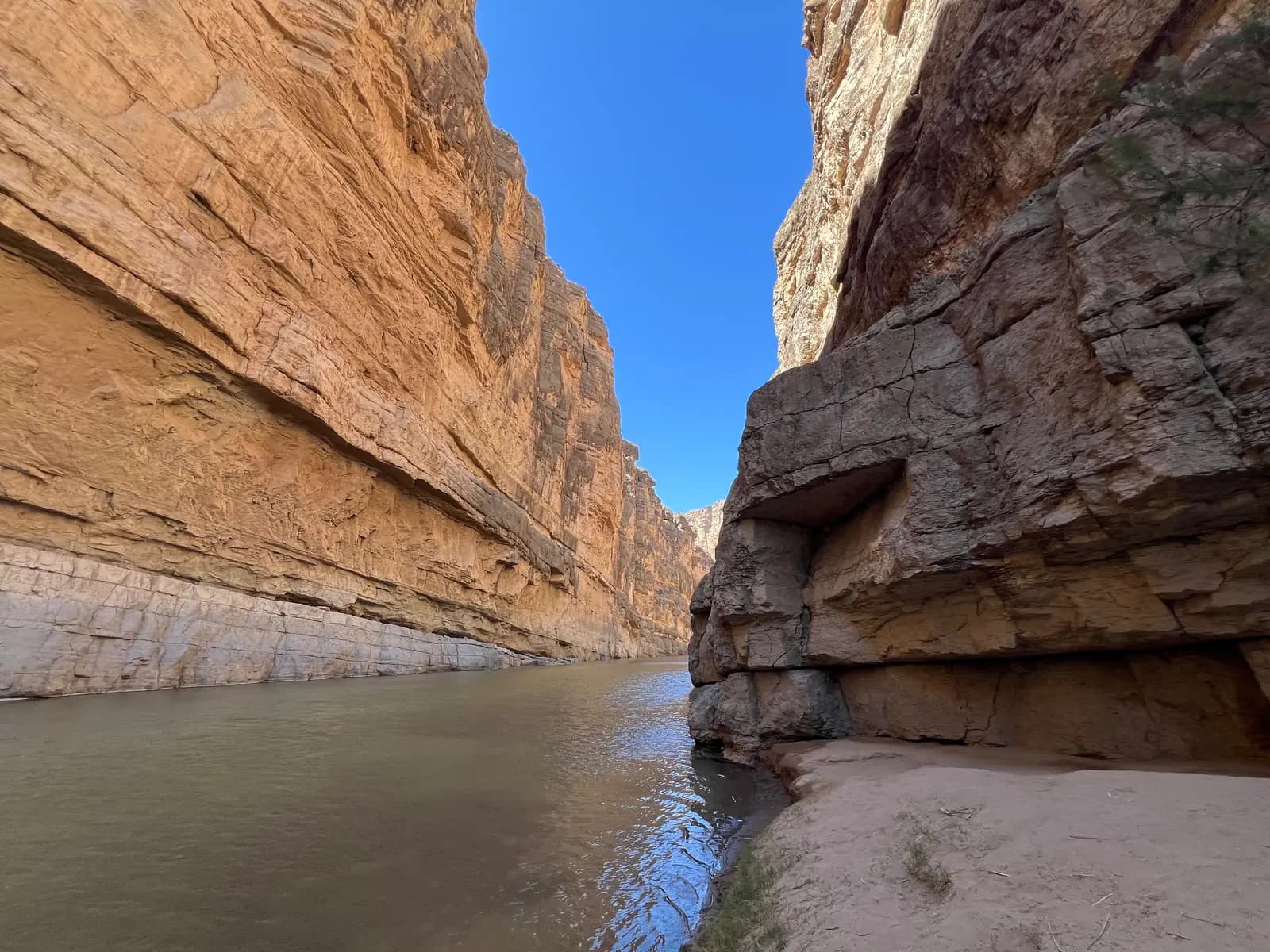 A low-angle view of the Rio Grande river flowing through the narrow, steep limestone cliffs of Santa Elena Canyon.