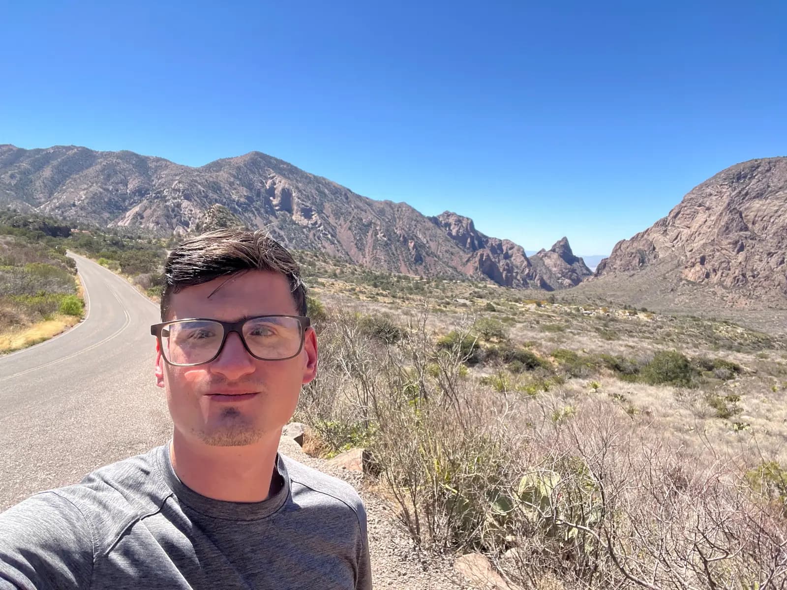 A view from a stone-lined overlook showing a rugged mountain range and desert plants under a vibrant blue sky.