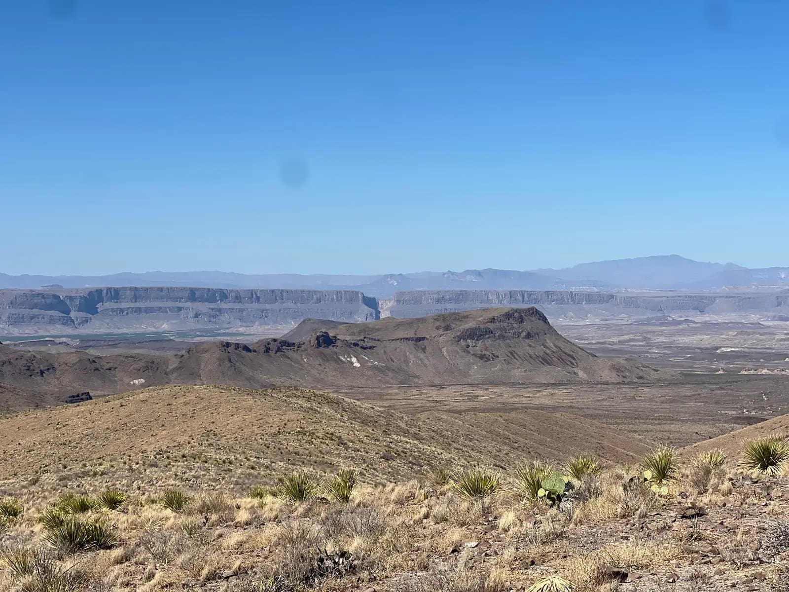 A wide desert vista looking toward a distinct narrow notch in a distant, flat-topped mountain range.