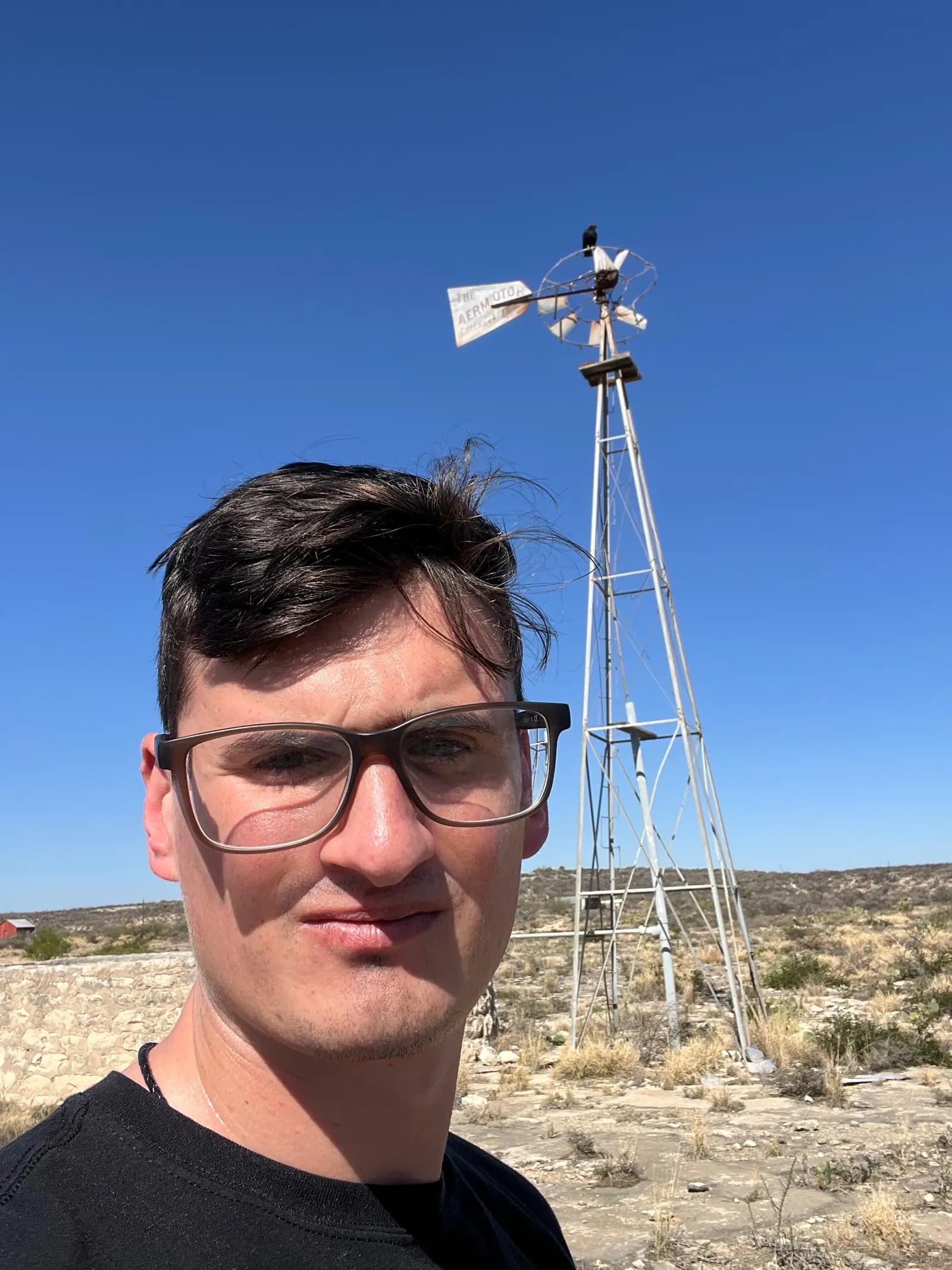 A self-portrait selfie with a vintage Chicago Aermotor windmill and the surrounding desert landscape.