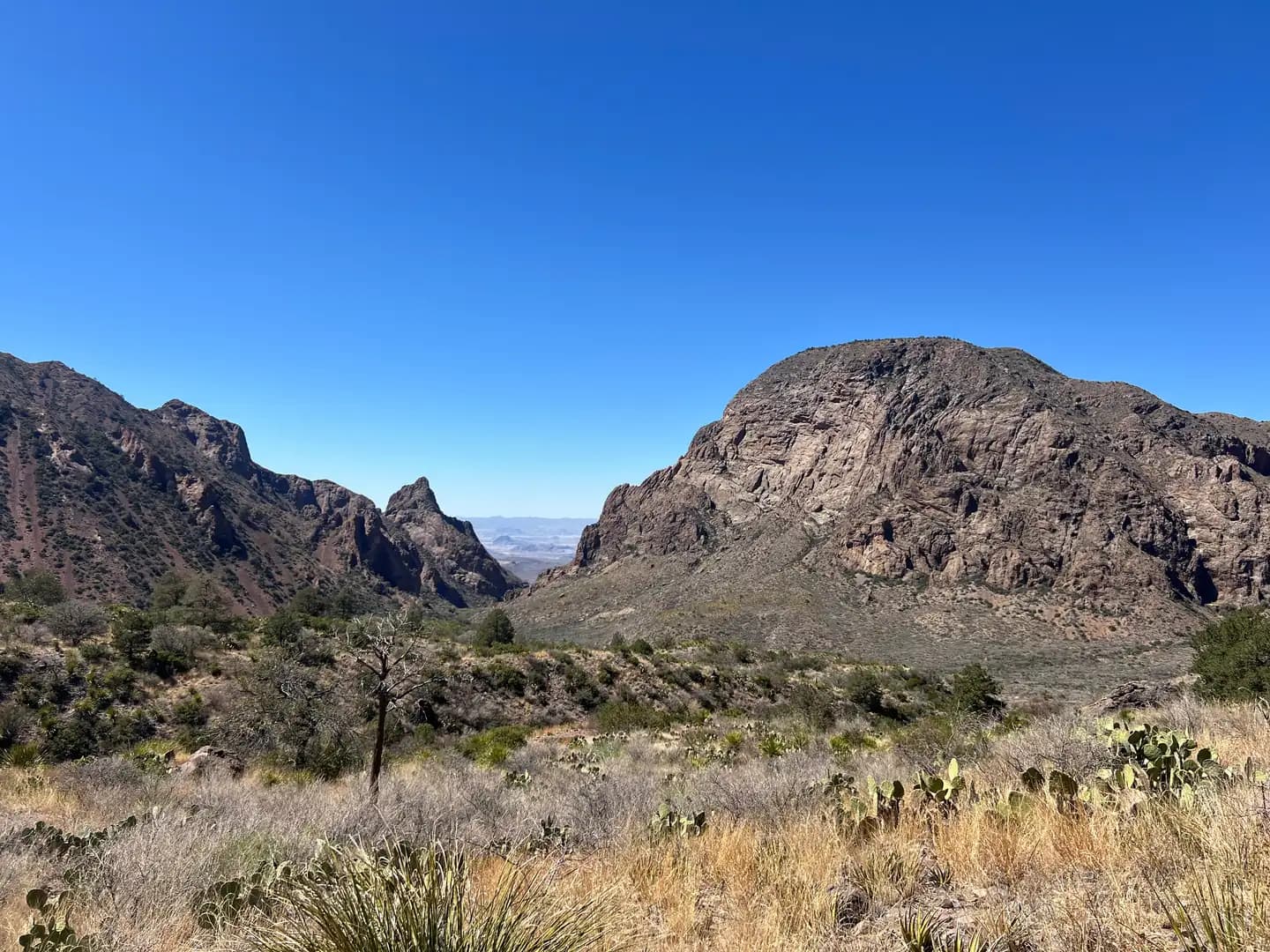 A scenic landscape view showing a V-shaped gap between two large mountains, revealing a distant desert horizon.
