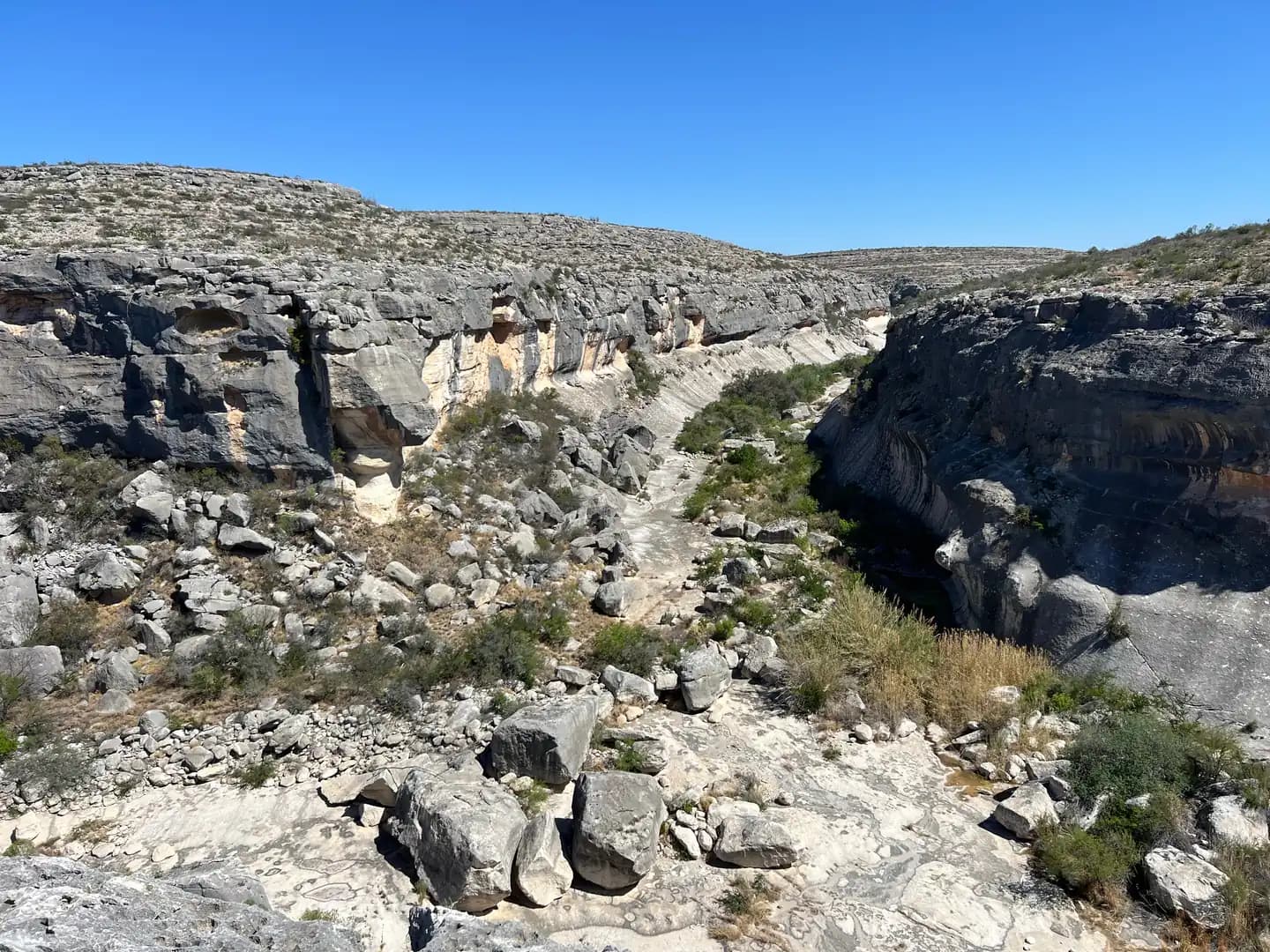 A vast, rocky canyon with large grey and tan limestone cliffs on both sides, enclosing a green, vegetated canyon floor.