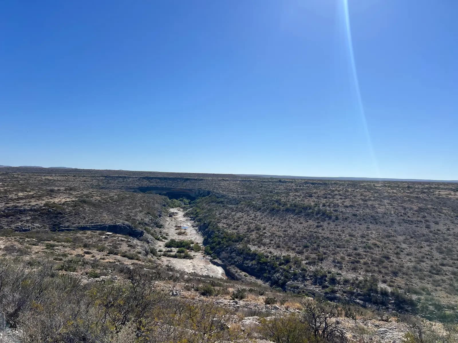 Looking across the wide, flat, brush-covered desert landscape toward the deep trench of Seminole Canyon.