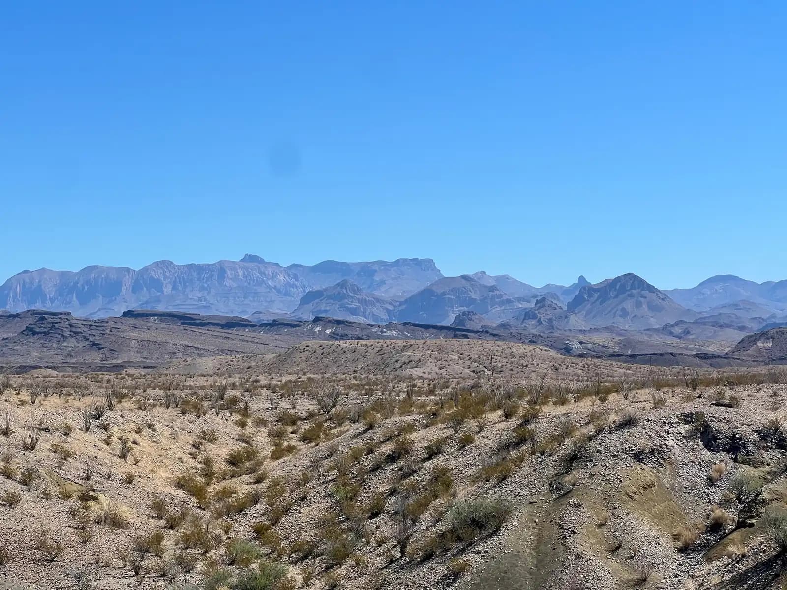 A panoramic view of rolling desert hills transitioning into a massive, jagged mountain range.