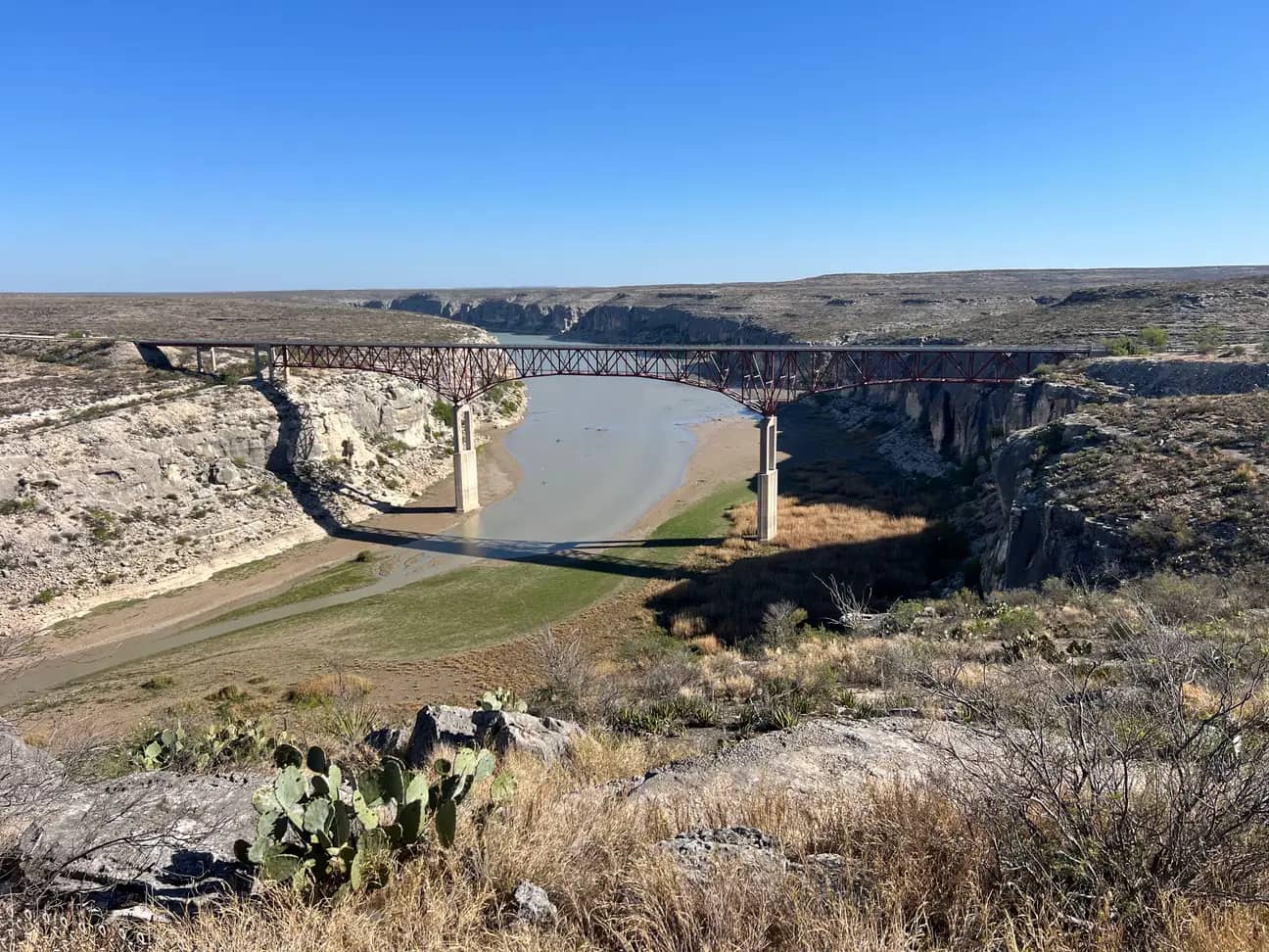 n elevated viewpoint looking down at the red, multi-span steel truss Pecos River High Bridge in West Texas.