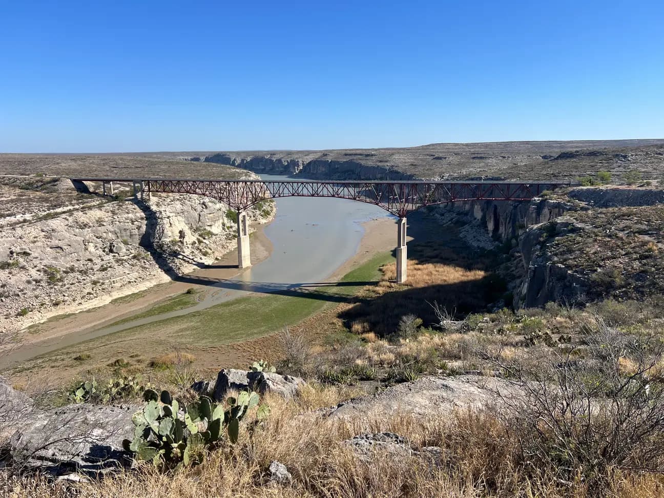 n elevated viewpoint looking down at the red, multi-span steel truss Pecos River High Bridge in West Texas.